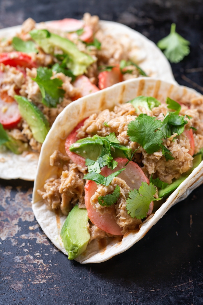 Fake crab tacos on a black plate with vegetables on top. 