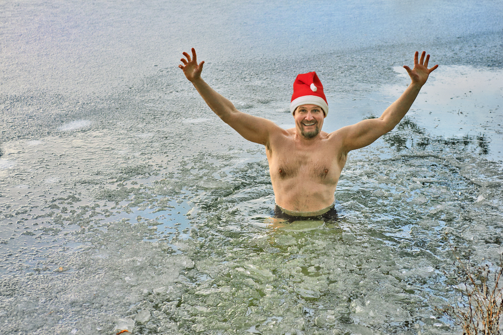 Winter bather in a Santa's hat stays in a frozen lake