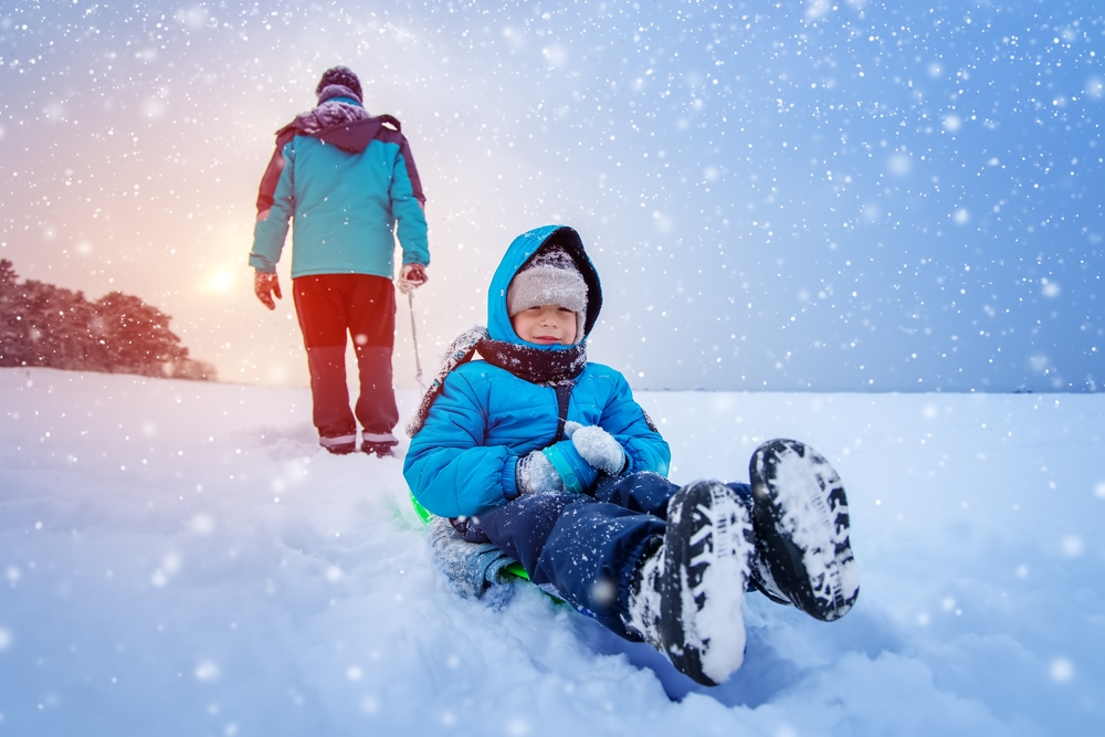 Father pulling sled with his lovely smiling son in snowfall. 