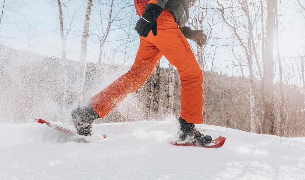 Snowshoeing people in winter forest mountain in snow. Man on hike in snow hiking in snowshoes living in winter on snowy day. Legs and snowshoe closeup