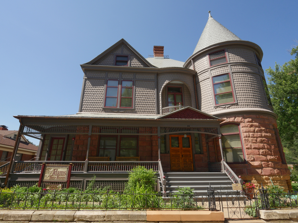 Front of the dark colored, historic Adams House with bricks and tower.