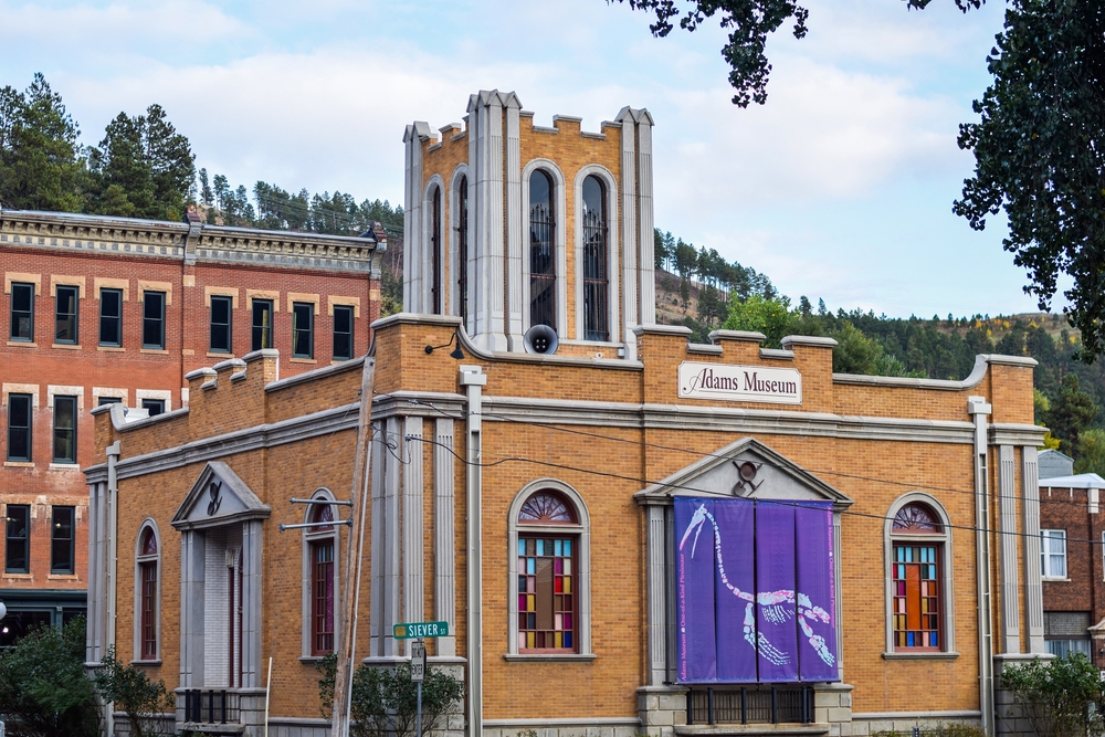 The exterior of the Adams Museum with stained glass windows and sign with a plesiosaur fossil.