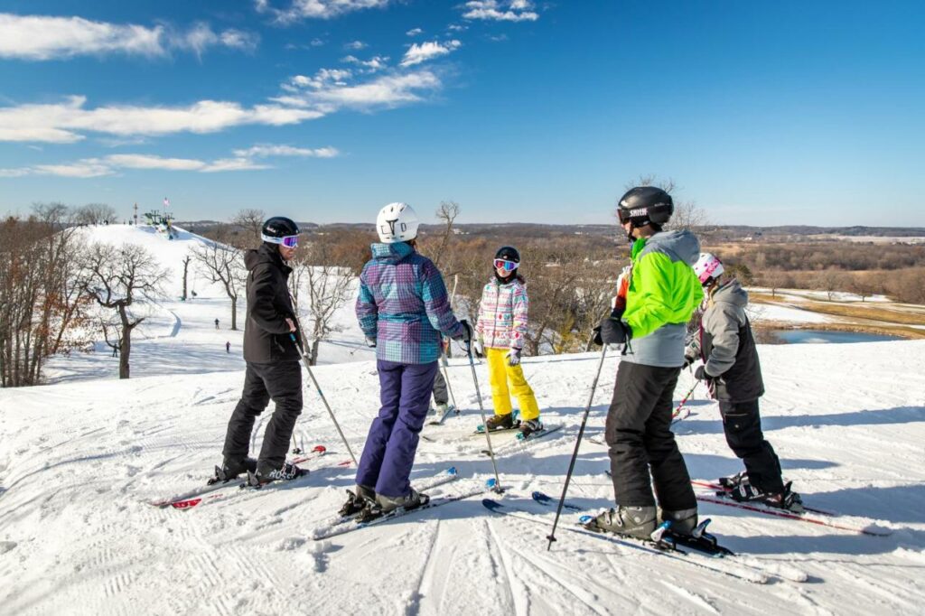 A group of people on skis stand at the top of a snowy ski hill in Wisconsin.