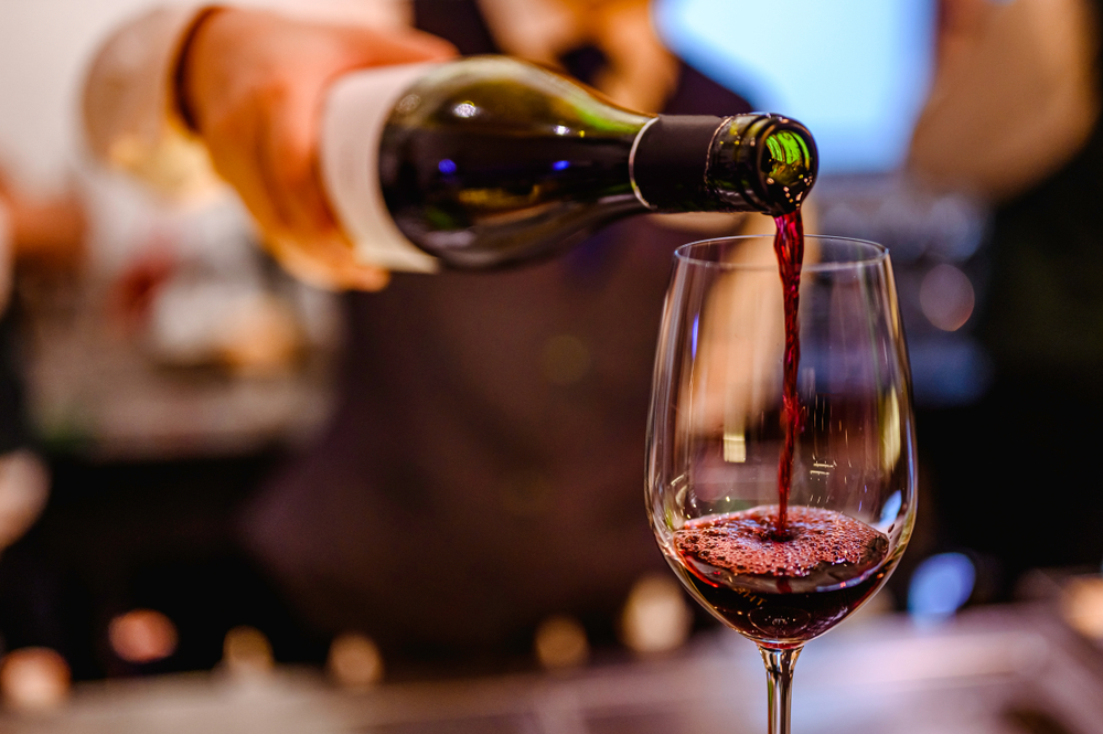 Bottle of red wine being poured into a glass at a bar.