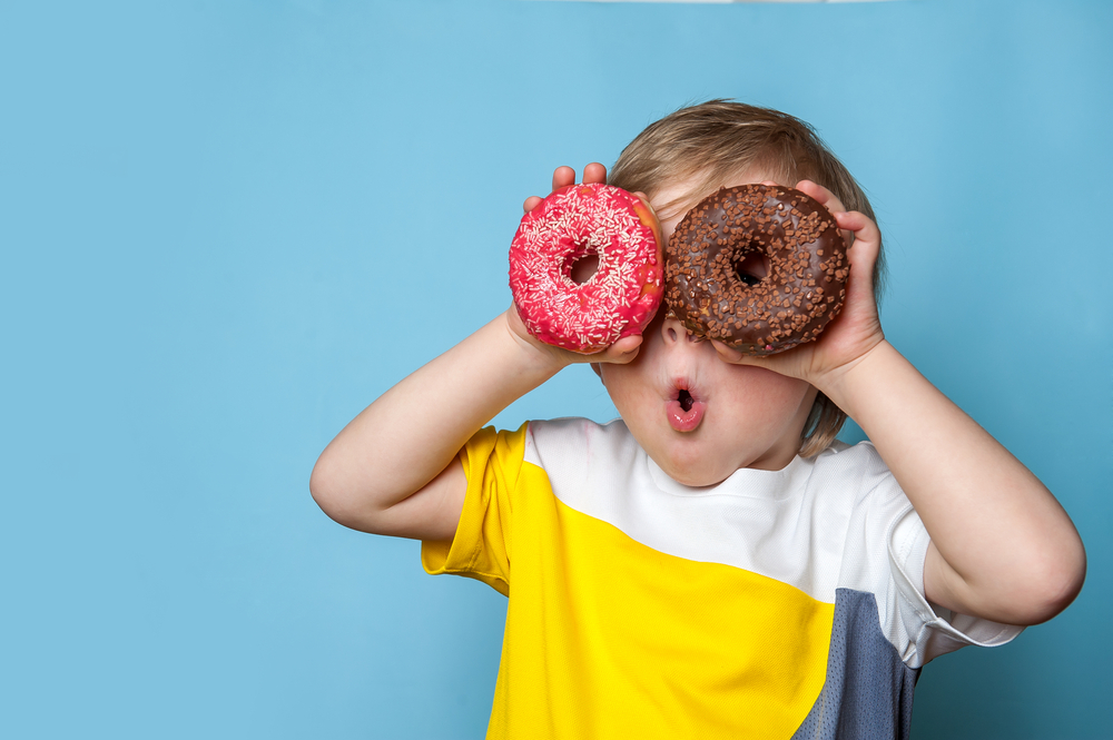 A kid holding up two donuts, one red one chocolate, to their eyes on a blue background