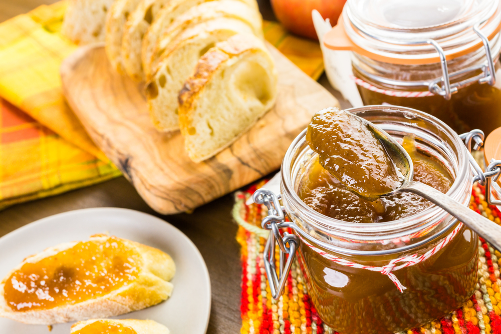 Jars of apple butter with fresh bread and a plate with bread and apple butter on it