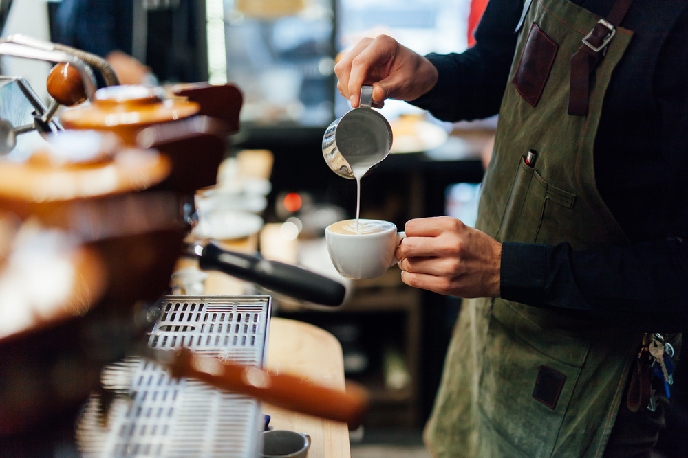 A barista in a green industrial apron pouring cream into a latte at one of the best coffee shops in Chicago