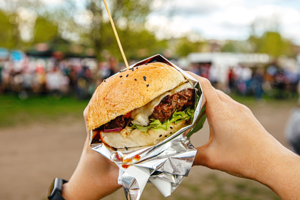 A person holding a chicken sandwich with a food truck festival in Ohio happening in the background