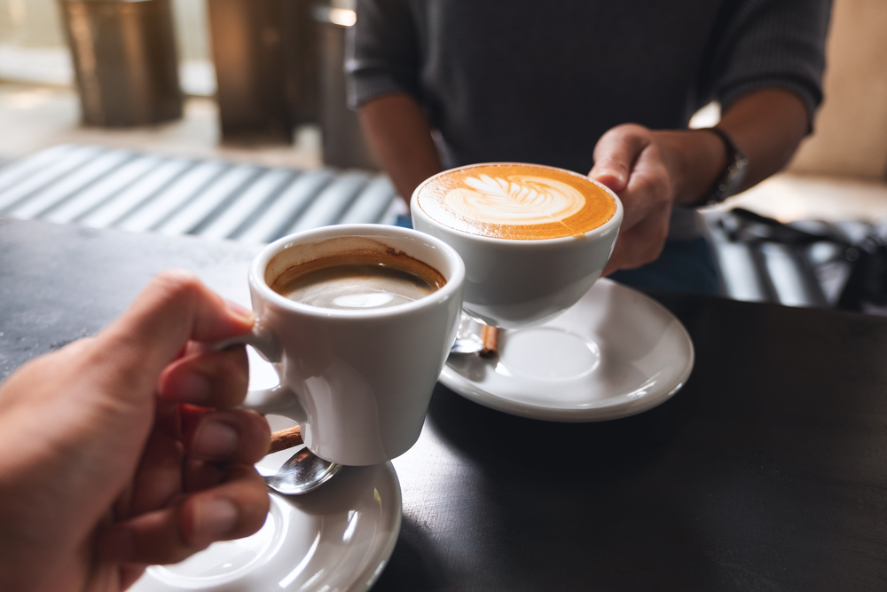 Two people clinking their white coffee mugs together