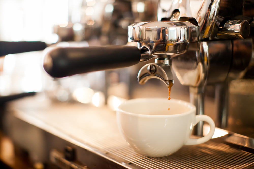 A close up of an industrial espresso machine dripping coffee into a white mug