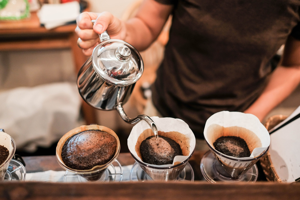 A barista pour water into three separate pour-over coffee makers