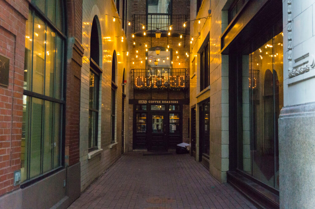 The front exterior in an alley of one of the best coffee shops in Chicago. There are string lights in the alley, and a large lit sign that says 'coffee'