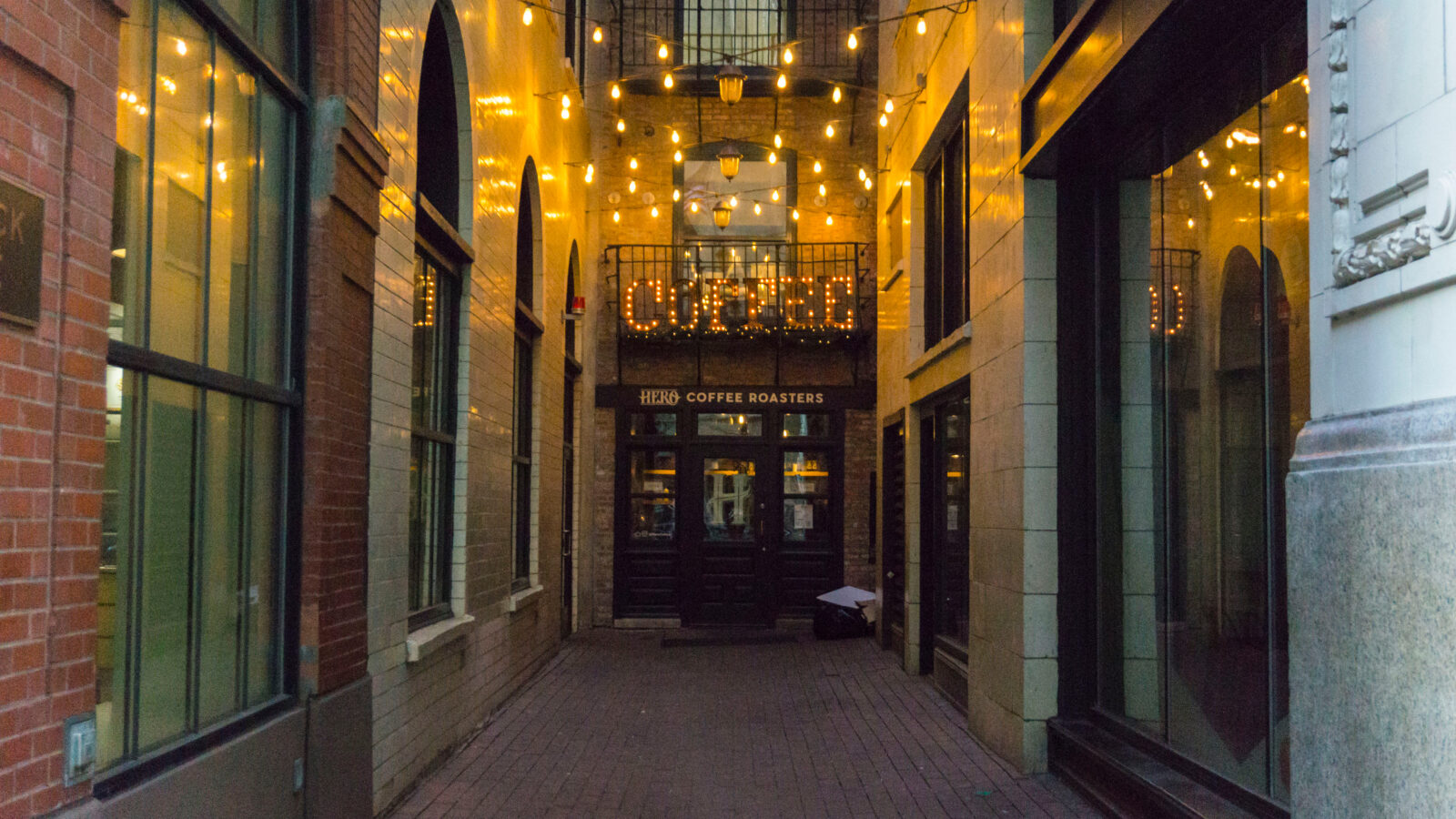 The front exterior in an alley of one of the best coffee shops in Chicago. There are string lights in the alley, and a large lit sign that says 'coffee'