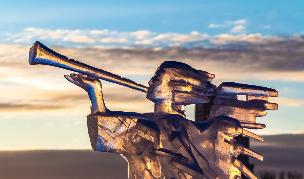 An ice sculpture that is an angel with a trumpet with the sky in the background