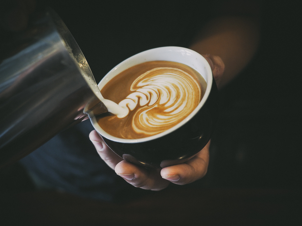 A closeup of a barista pouring cream into a latte to make latte art
