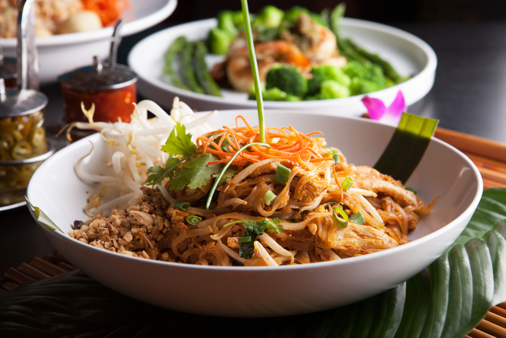 a bowl of chicken pad thai with a variety of veggies served on a table