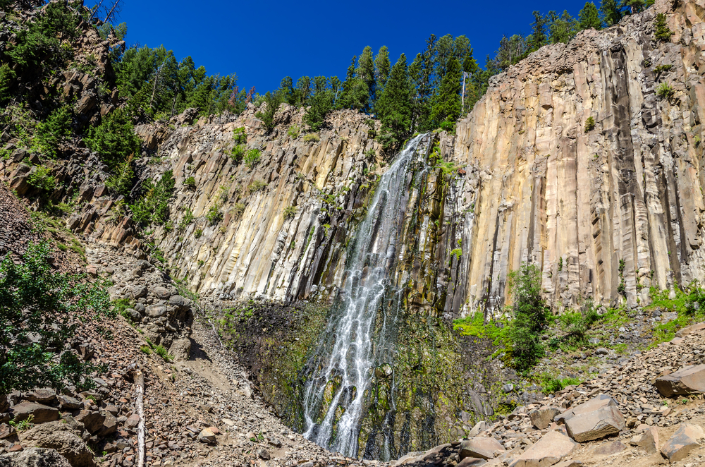 A large cascading waterfall on the side of a rocky cliff on a sunny day, one of the best things to do in Bozeman