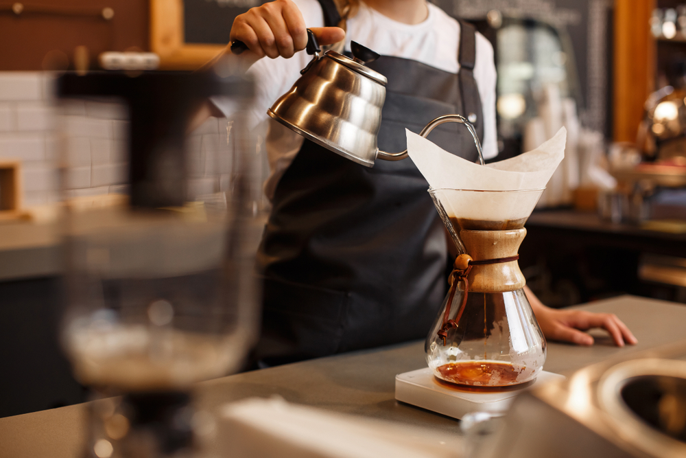 A barista pouring water into a single glass pour-over container