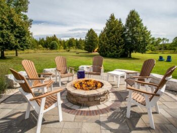 Resorts in Door County chairs around fire pit with green grass and trees in background.