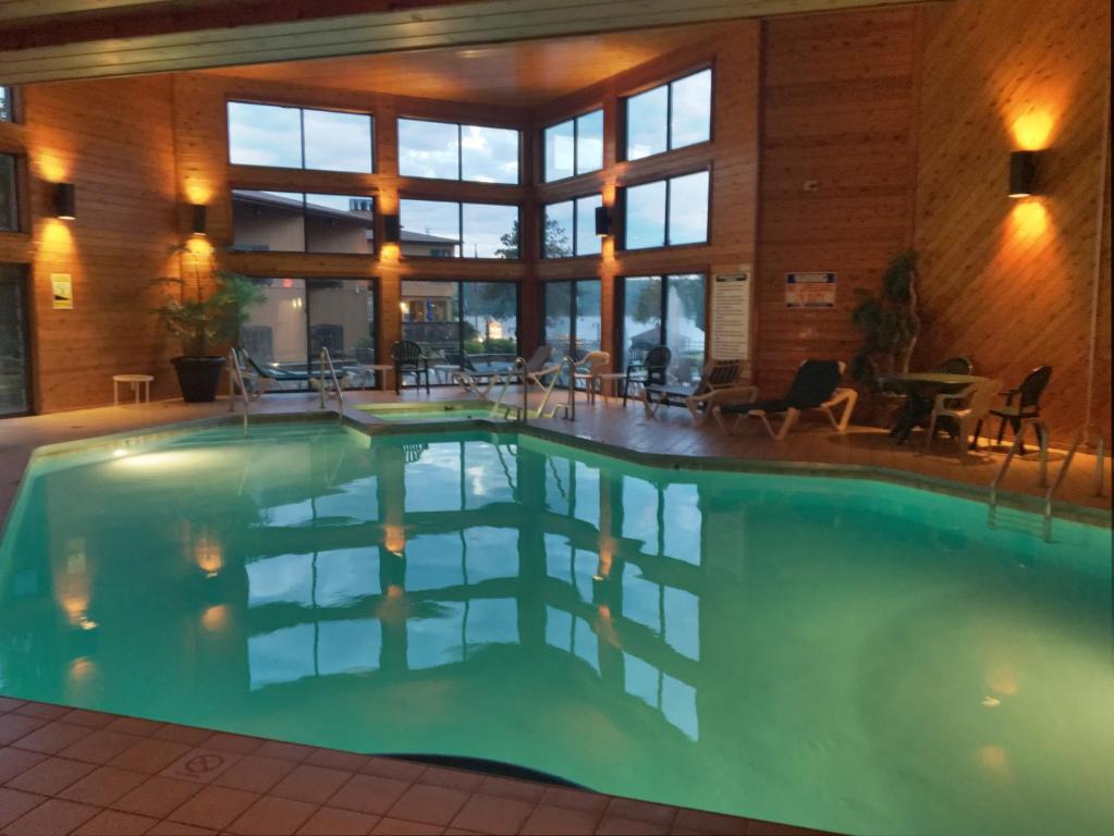 Swimming pool in a wood style cabin with huge windows. The pool has loungers around it and a whirl pool area. 