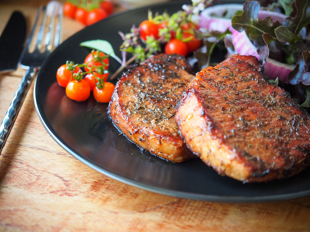 well done grilled pork chop steak on a black plate with tomatoes