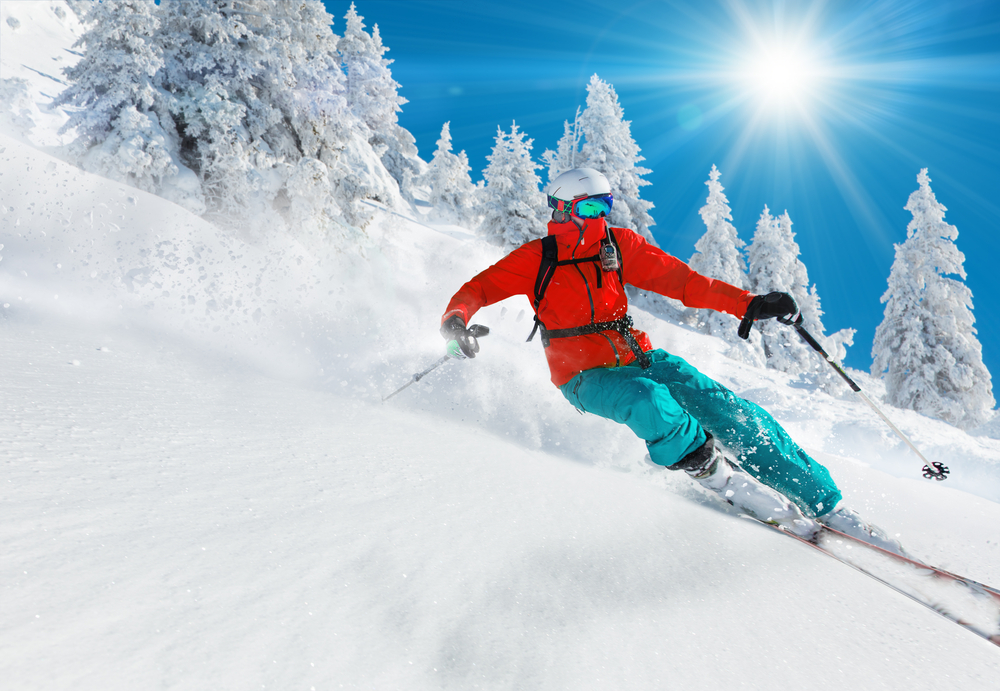 A person skiing in a red jacket and blue pants on a snowy mountainside on a sunny day
