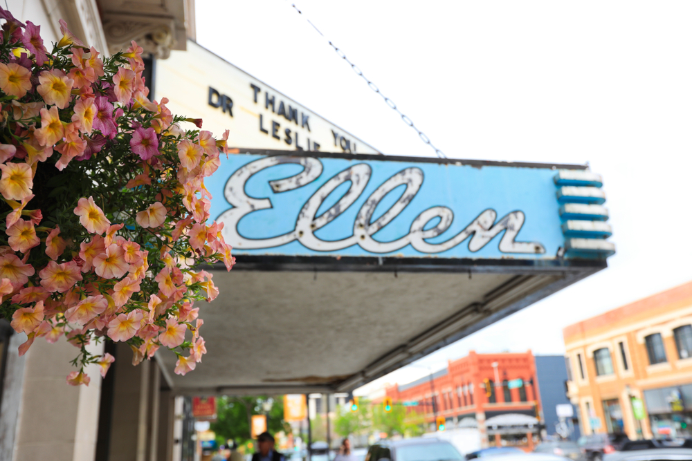 The original marque for the Ellen Theater that is pale blue with peach and pink petunias next to it