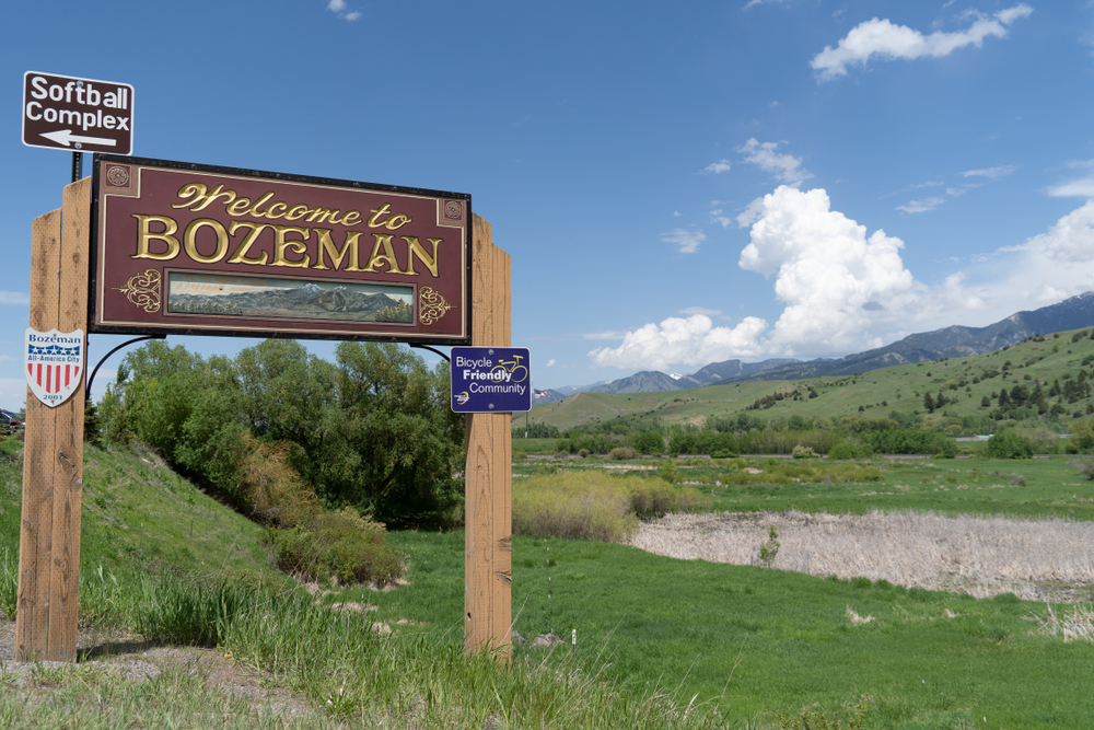 A wooden sign welcoming you to Bozeman Montana near a valley and mountains on a sunny day
