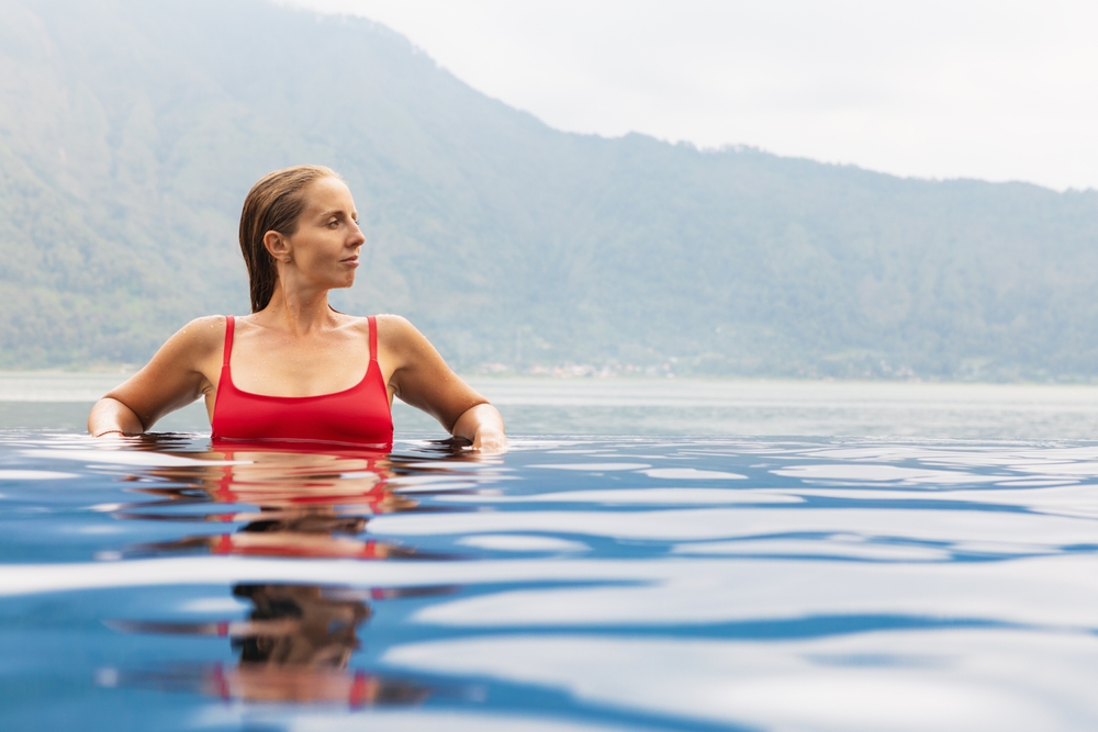 A woman in a red bathing suit relaxing in a hot spring with mountains in the background