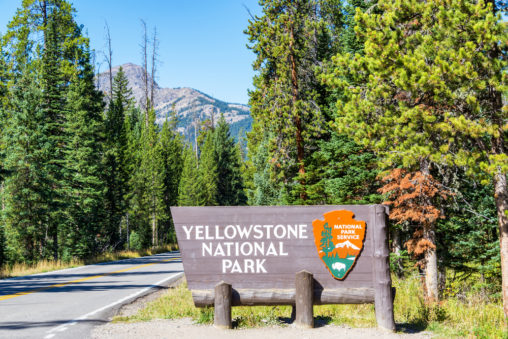 A sign welcoming you to Yellowstone National Park with mountains and trees in the background