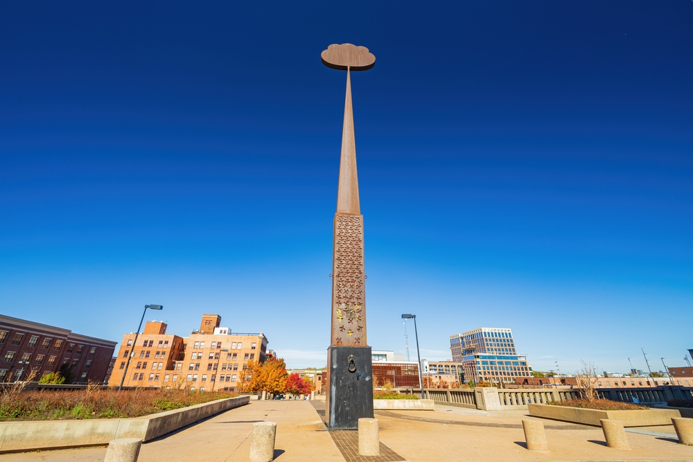 A tall sculpture that is a narrow rod that leads to a cloud shape in a park in Tulsa OK.