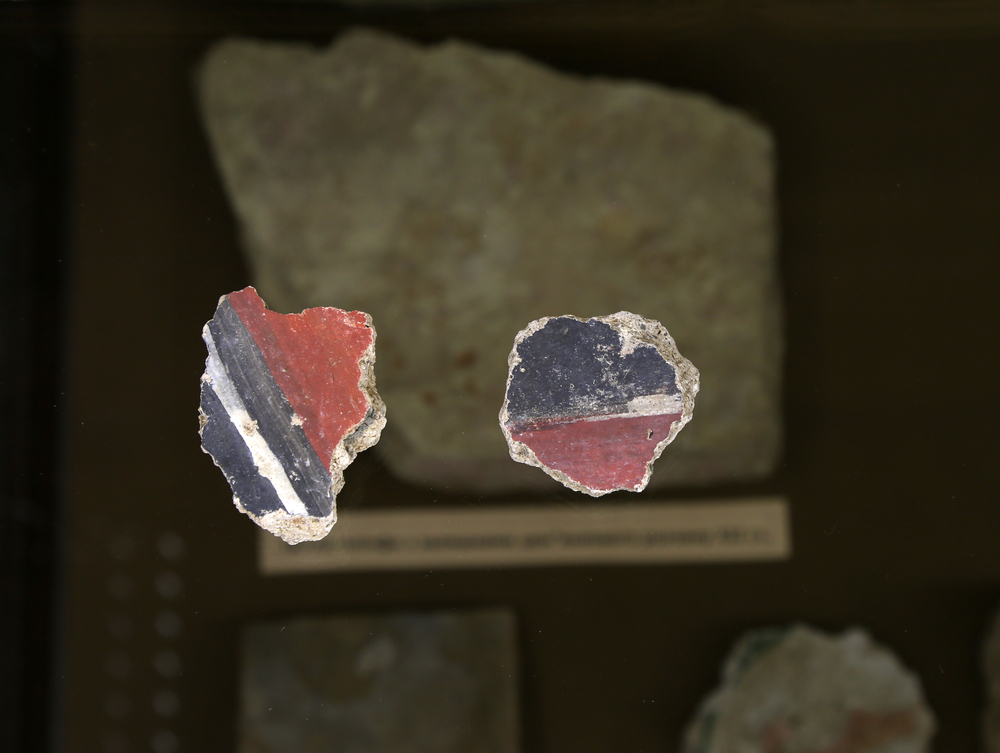 Two pieces of Jewish pottery that are painted blue, red, and white, on display in a museum with other artifacts in the background