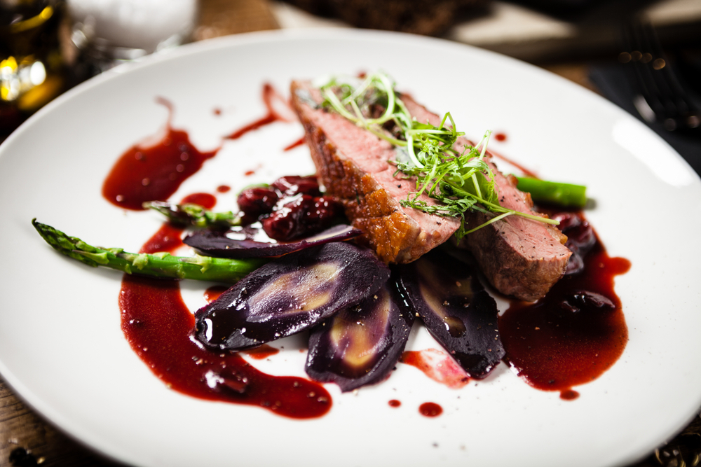 A plate at a fine dining restaurant in Tulsa that is plated with seared duck breast, red wine sauce, asparagus, and artichokes. 