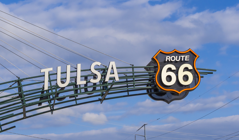 A sign hanging in the air that says Tulsa with the Route 66 sign on a sunny day