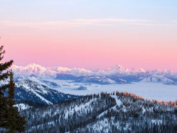 orange colored sky over snow covered forest and mountains winter in montana