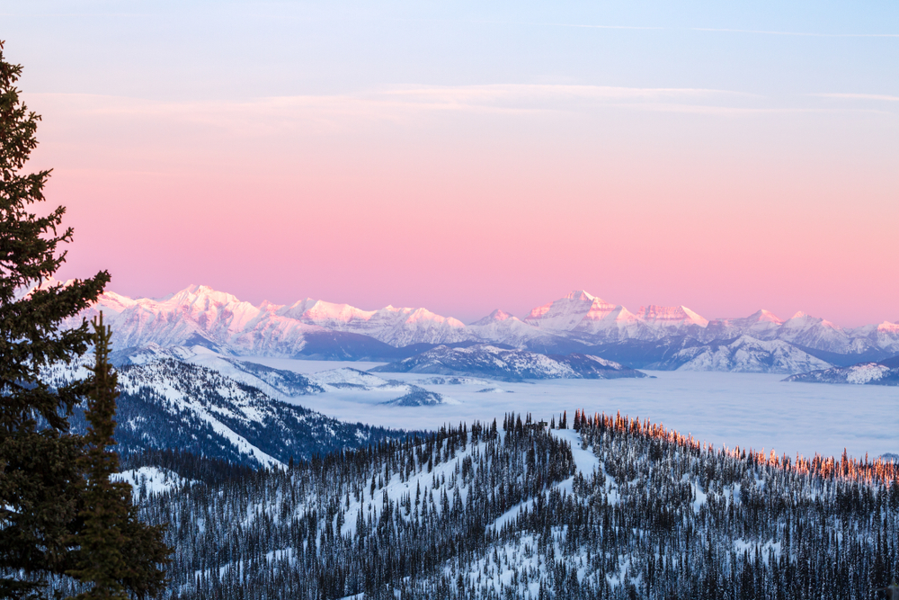 orange colored sky over snow covered forest and mountains winter in montana