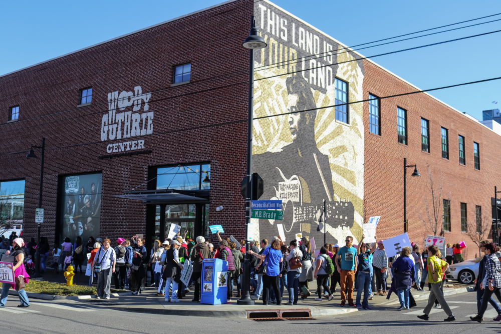 The exterior of the Woody Guthrie Center, a large brick building with people protesting in front of it. It's one of the best things to do in Tulsa Oklahoma