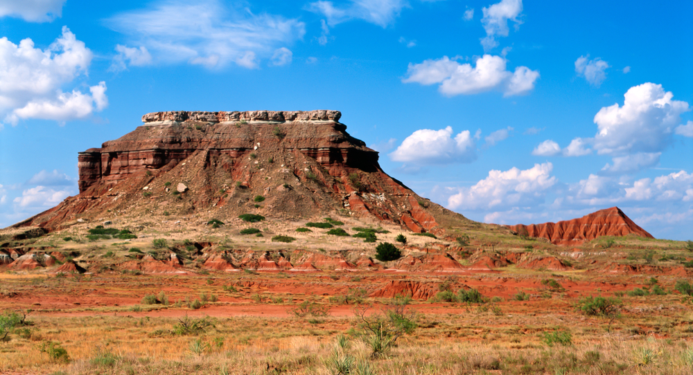 View across a plain to a towering  red rock mesa in Gloss Mountain State Park.