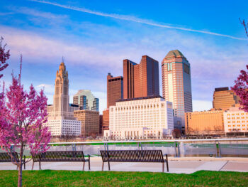 View of the Columbus skyline with flowering trees in the foreground during spring in Ohio.