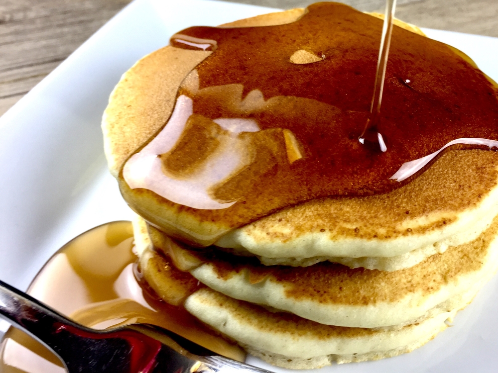 A pile of pancakes getting drizzled with maple syrup.