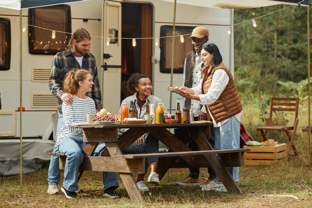 A group of people sitting at a picnic table eating outside of an rv in the woods while camping in Oklahoma