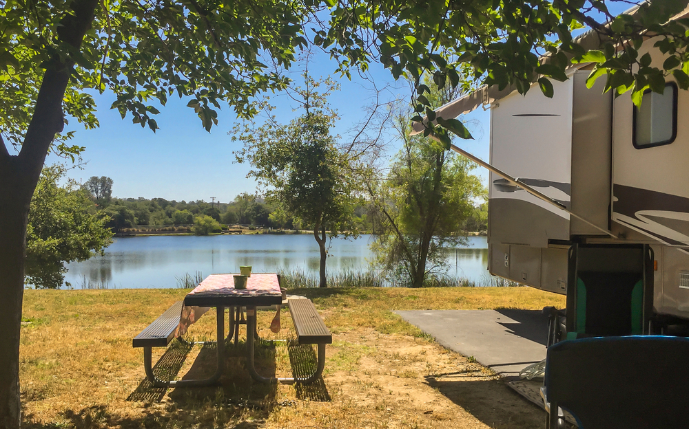An RV on a concrete pad with views of a lake surrounded by trees