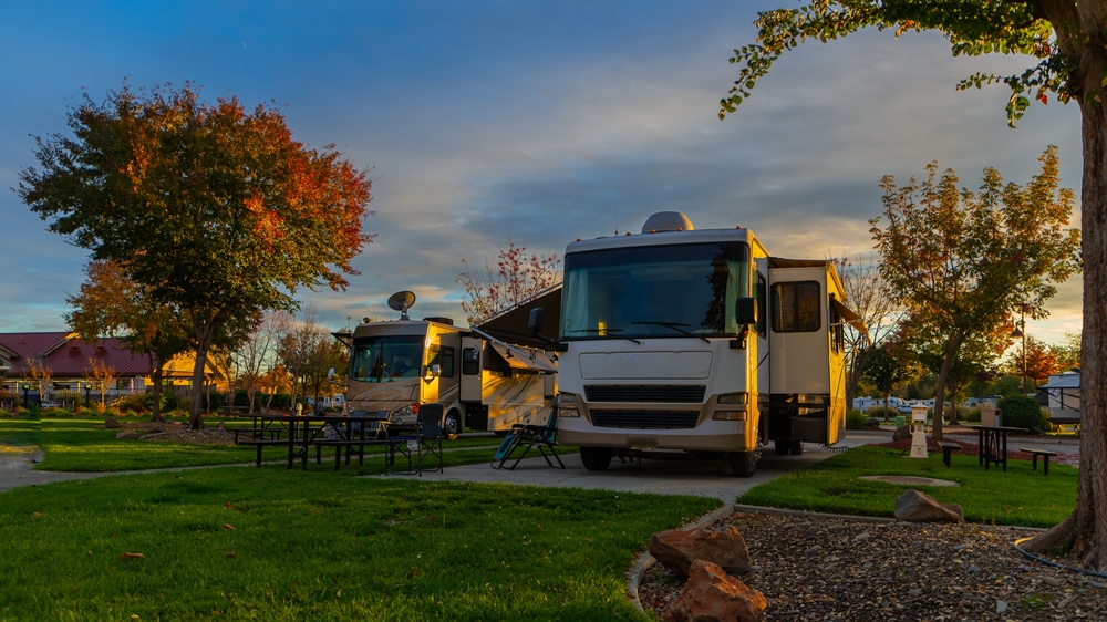 A group of RVs at an RV campground where there is grass, trees, and picnic tables