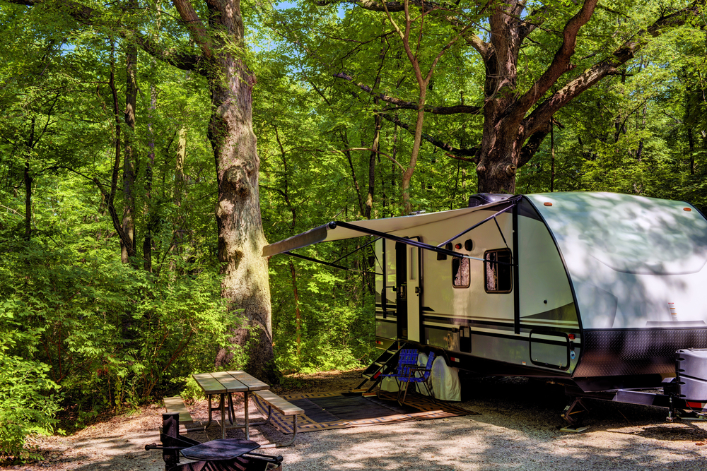 An RV on gravel surrounded by trees in the woods