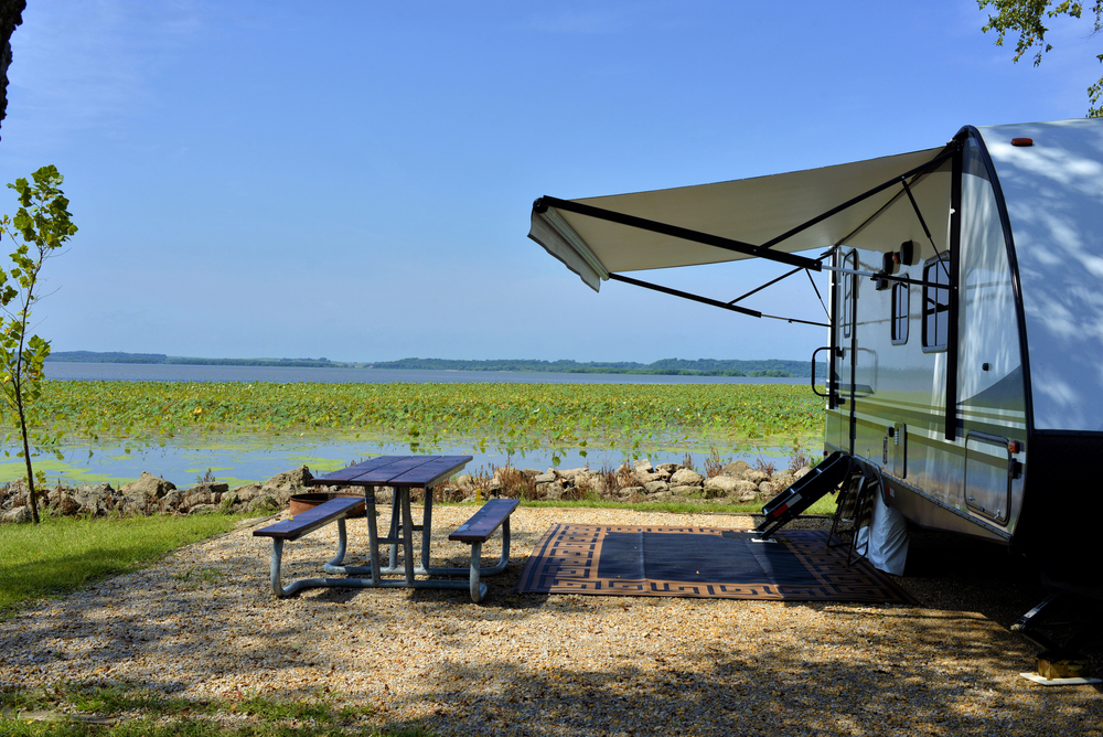 An rv set up on the shores of a river full of greenery with a picnic table next to it