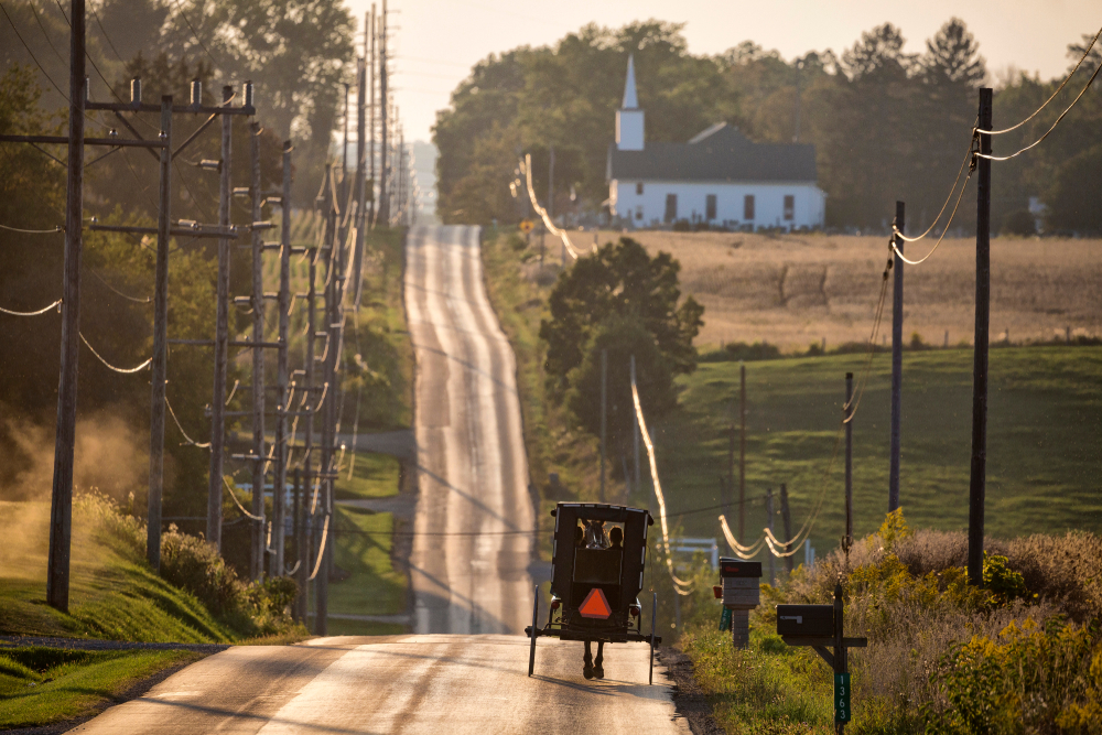Amish trolly going down the road with a church in the background