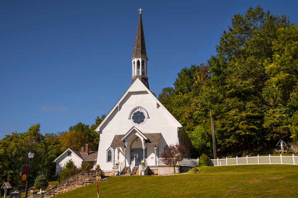 This image shows the front view of an old idyllic rural, small town church chapel building on top of a green hill. French Lick is one of the things to do in midwest 