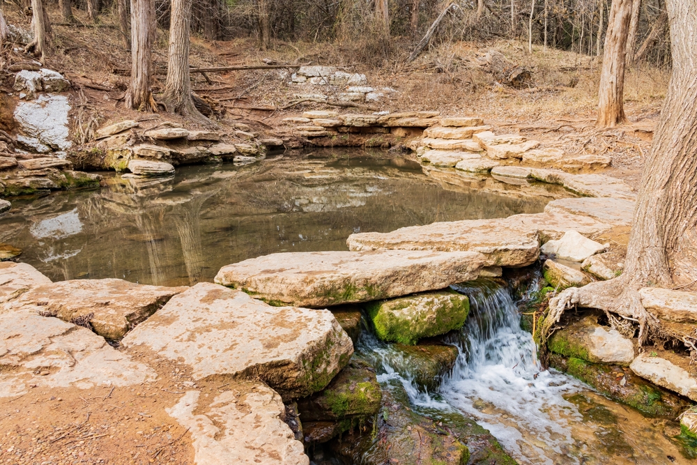 One of the springs at Roman Nose State Park surrounded by stones and a waterfall.