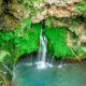 Nature alcove with green moss growing on rock walls and cancading water fall down to blue pool of water
