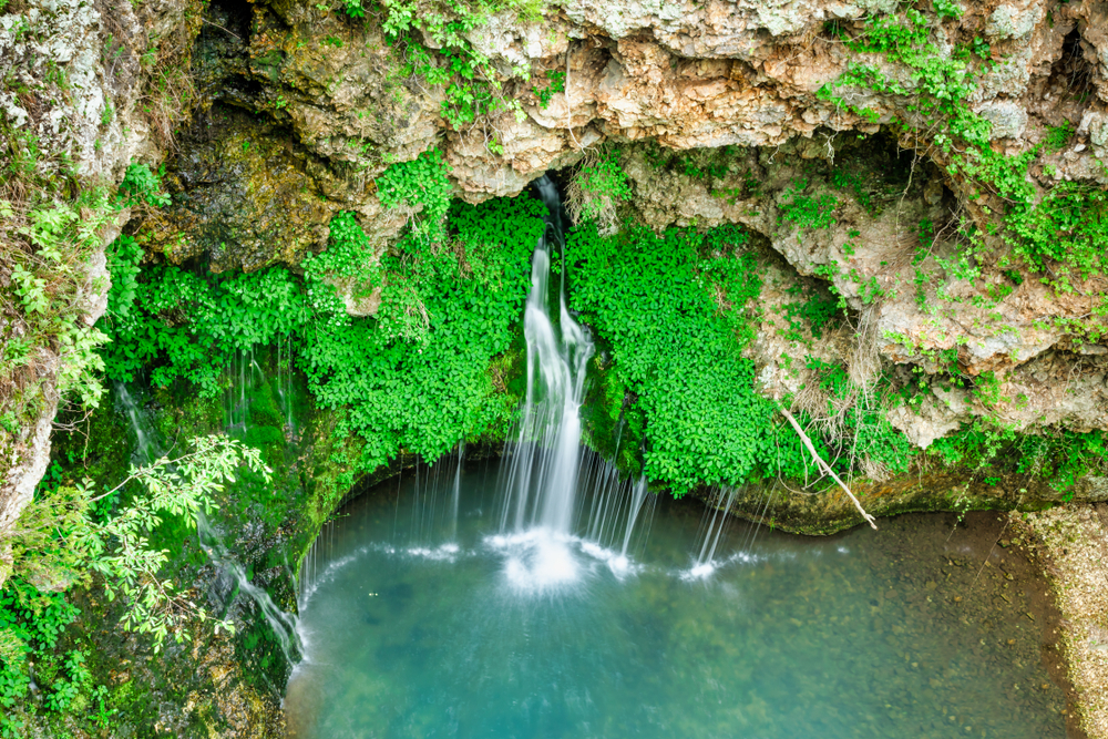 View looking down at Dripping Springs in Oklahoma with a waterfall and greenery.